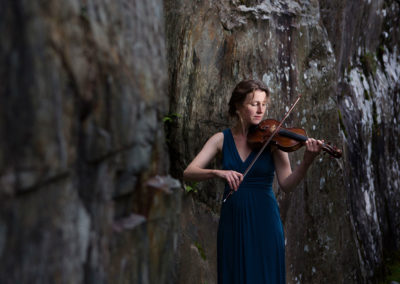 a woman plays a violin surrounded by rocks by Anglesey commercial photographer Gill Jones Photography