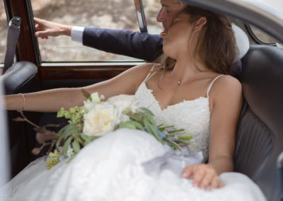 bride and groom sitting in the back of their wedding car, the bride rests her head against the groom's shoulder by Anglesey wedding photographer Gill Jones