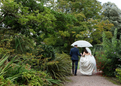 bride and groom walking under a white umbrella in Chateau Rhianfa's gardens