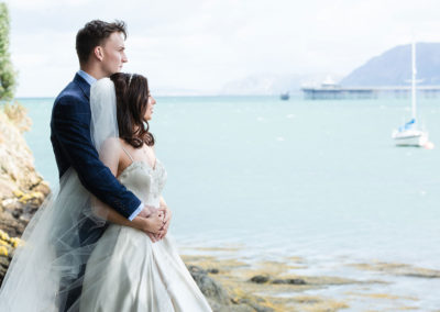 bride and groom hugging looking out at the Menai Straits at Chateau Rhianfa