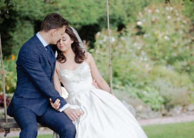 bride and groom sitting on a swing in the gardens of Chateau Rhianfa