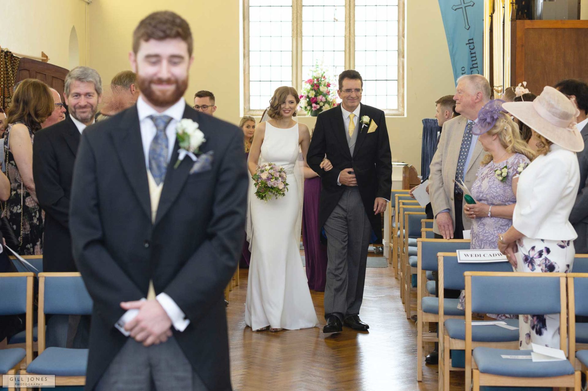 the bride is approaching her grrom up the aisle of St. Ffraids in Trearddur Bay