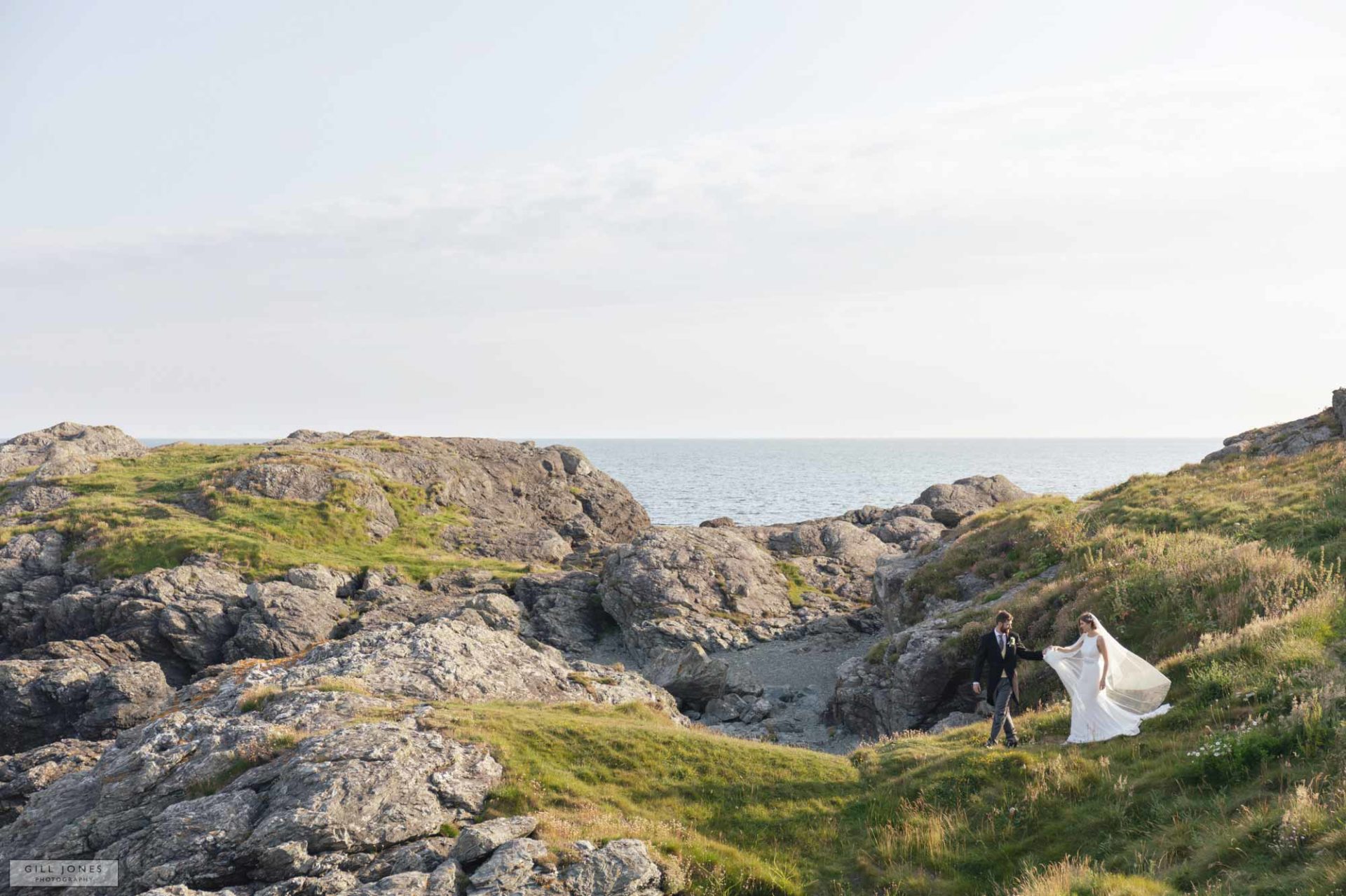 the groom leads his bride along the rocks in trearddur bay