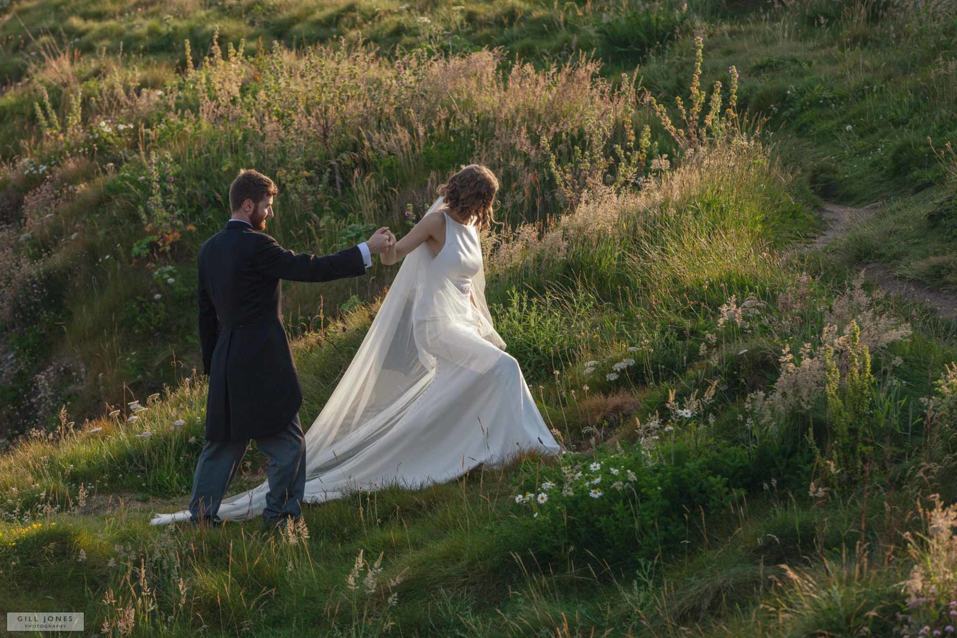 a groom is helping his wife along the rocks in trearddur bay