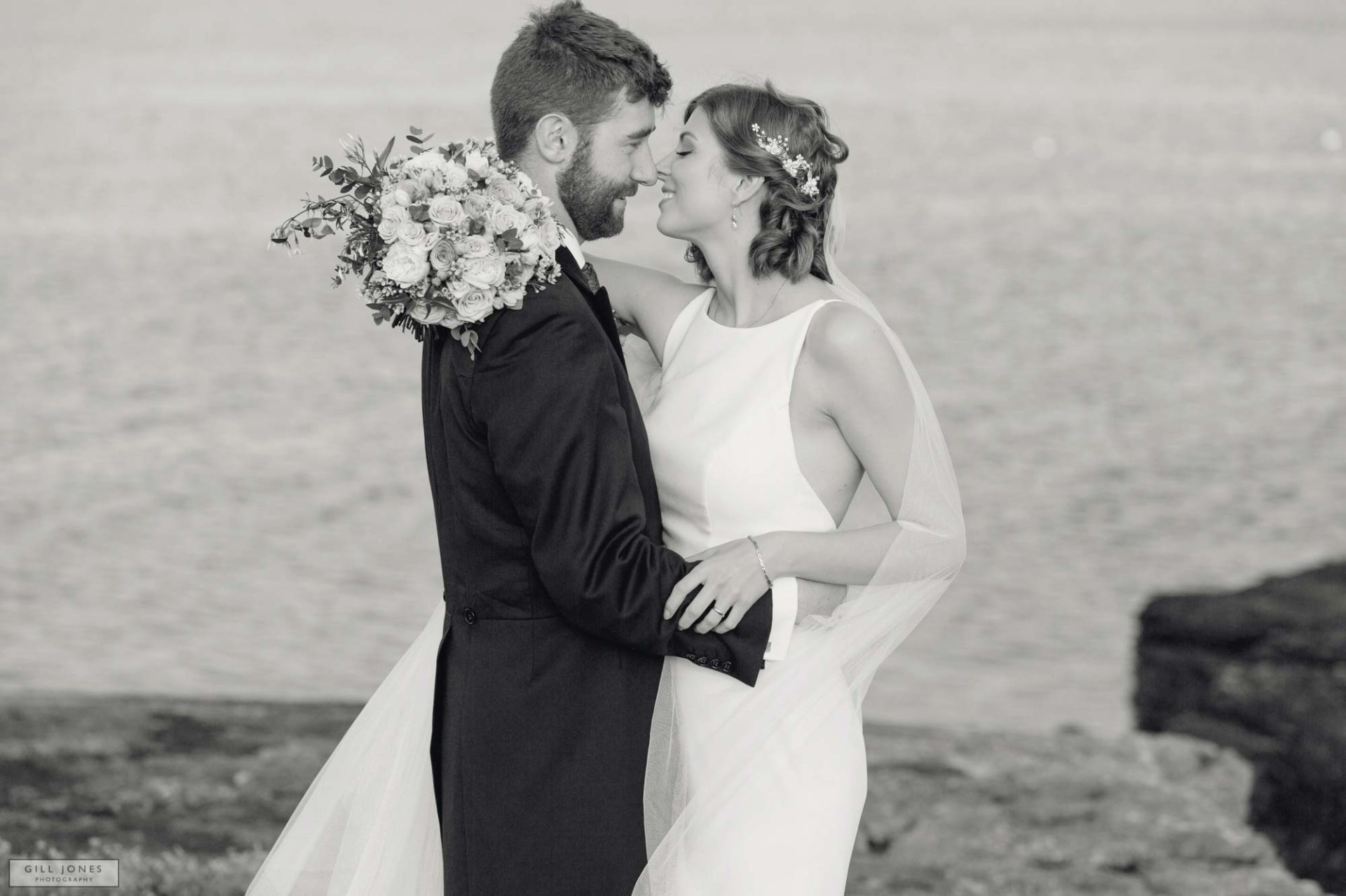 anglesey bride and groom caressing on the rocks in Trearddur Bay