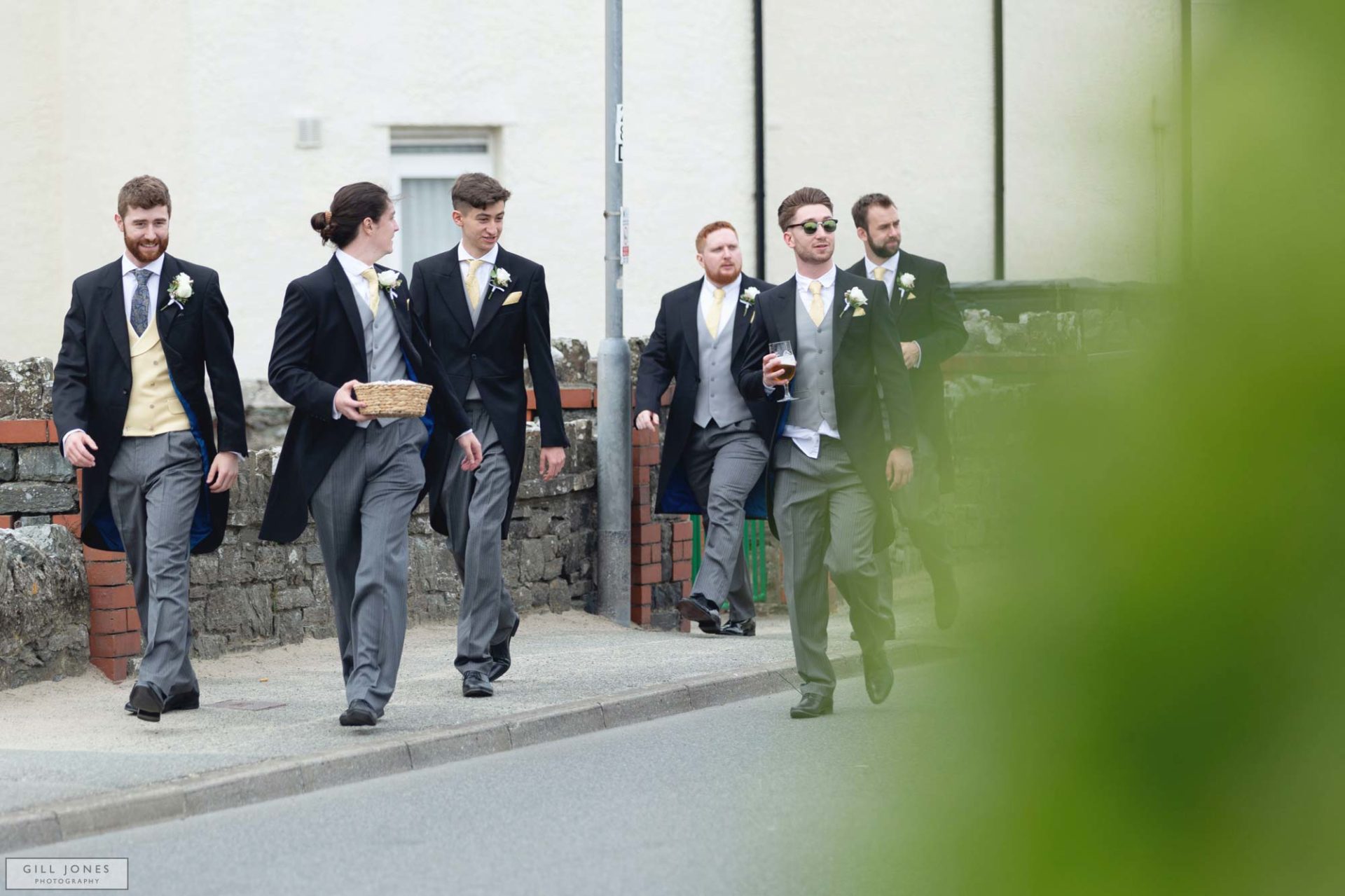 grooms men are walking along the road in Trearddur Bay towards St. Ffraids church