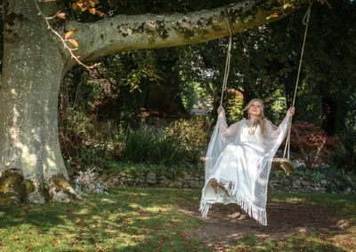 bride swinging on the swing that hangs from tree in the gardens of Chateau Rhianfa by Anglesey wedding Photographer Gill Jones