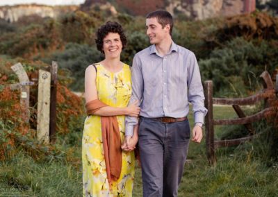 Holyhead mountain in the background as couple walk along path at Holyhead Breakwater Parkcouple sitting side by side on steps around Holyhead Break water park by Anglesey wedding photographer Gill Jones