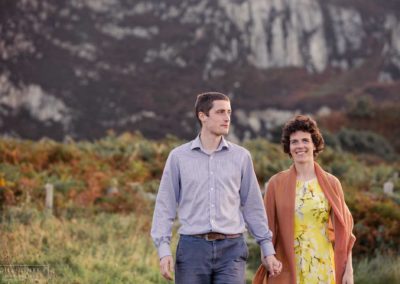 Holyhead mountain in the background as a couple walk together along a path at Holyhead Breakwater Parkcouple sitting side by side on steps around Holyhead Break water park by Anglesey wedding photographer Gill Jones