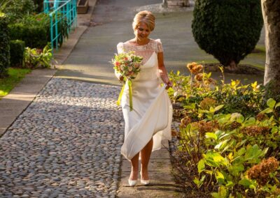 a bride walks through Portmeirion Village in the early morning sunshine she holds the hem of her skirt by Anglesey wedding photographer Gill Jones Photography