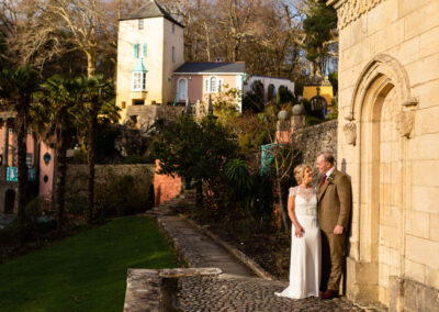 a bride and groom stand side by side against a sun kissed wall at Portmeirion Village by Anglesey wedding photographer Gill Jones Photography