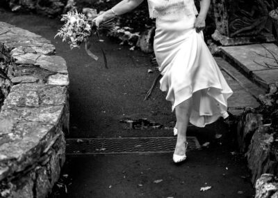 a bride jumps over a grid as she holds her dress up around her knees by Anglesey wedding photographer Gill Jones Photography