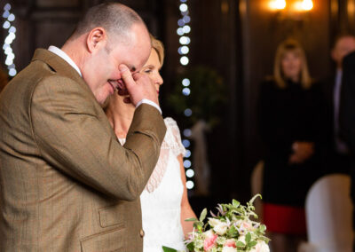 a groom is overcome with emotion and holds his hand over his eyes as his bride approaches him by Anglesey wedding photographer Gill Jones Photography