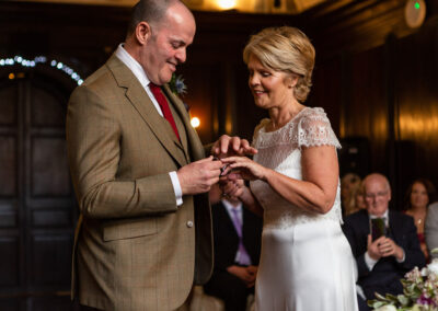 a groom is about to place a wedding ring on his bride's finger in Hercules Hall at Portmeirion Village by Anglesey wedding photographer Gill Jones Photography