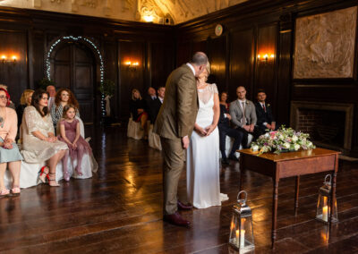 a groom kisses his bride at the end of a wedding ceremony in Hercules Hall at Portmeirion Village by Anglesey wedding photographer Gill Jones Photography