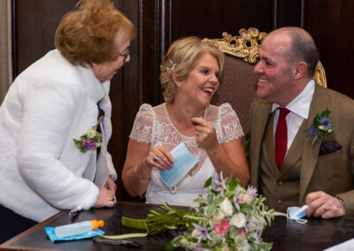 the brides mother chats with the bride and groom after they've signed the register in Hercules Hall at Portmeirion Village by Anglesey wedding photographer Gill Jones Photography