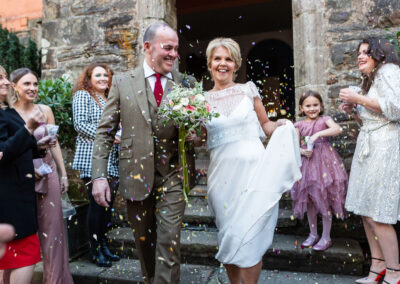 a bride and groom walk out of Hercules Hall at Portmeirion Village and confetti is thrown at them by guests by Anglesey wedding photographer Gill Jones Photography