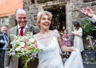 confetti is thrown at a bride and groom the bride raises her eyes to look at the guest by Anglesey wedding photographer Gill Jones Photography