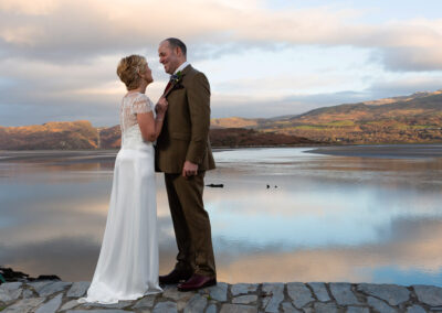 A couple at Portmeirion village stand close together, nose to nose with the Dwyryd Estuary in the background by Anglesey wedding photographer Gill Jones Photography