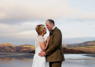 A coupe stand face to face with noses almost touching with a beautiful landscape opposite Portmeirion village in the background and the Dwyryd Estuary by Anglesey wedding photographer Gill Jones Photography