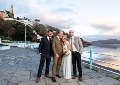 husband and wife with two young gentlemen standing on the banks of Dwyryd Estuary at Portmeirion Village by Anglesey wedding photographer Gill Jones Photography