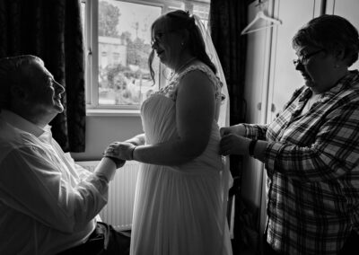 Mum ties wedding dress as father holds hands with daughter by Anglesey wedding photographer Gill Jones Photography