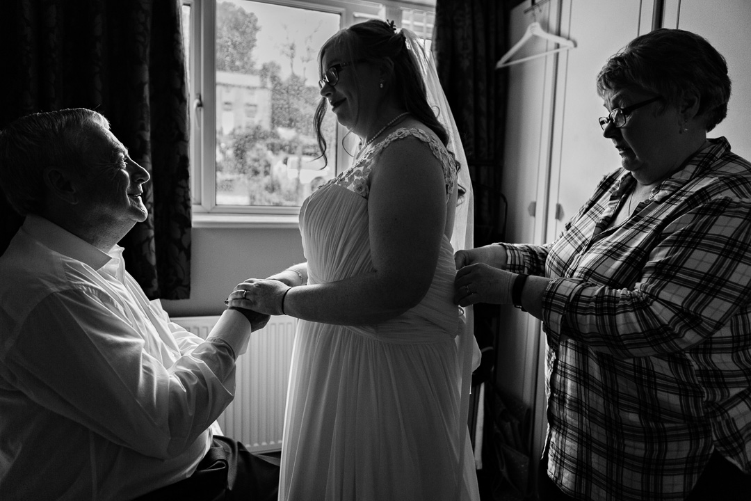 Mum ties wedding dress as father holds hands with daughter by Anglesey wedding photographer Gill Jones Photography