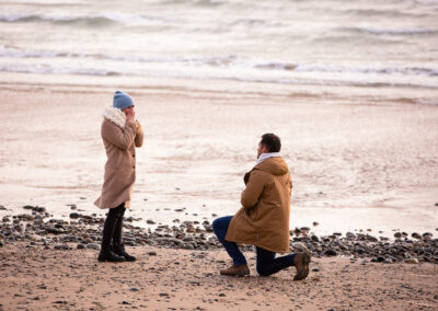 man kneeling before his girlfriend to propose Llanddwyn island