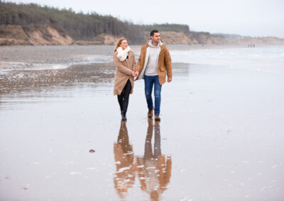 newly engaged couple walking along Newborough beach on Anglesey towards Llanddwyn Island by Anglesey wedding photographer Gill Jones