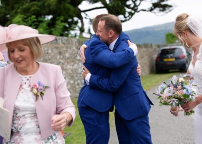 the groom receives a huge hug after the ceremonyat St. Mary's Church , Caerhun by Anglesey wedding photographer Gill Jones Photography