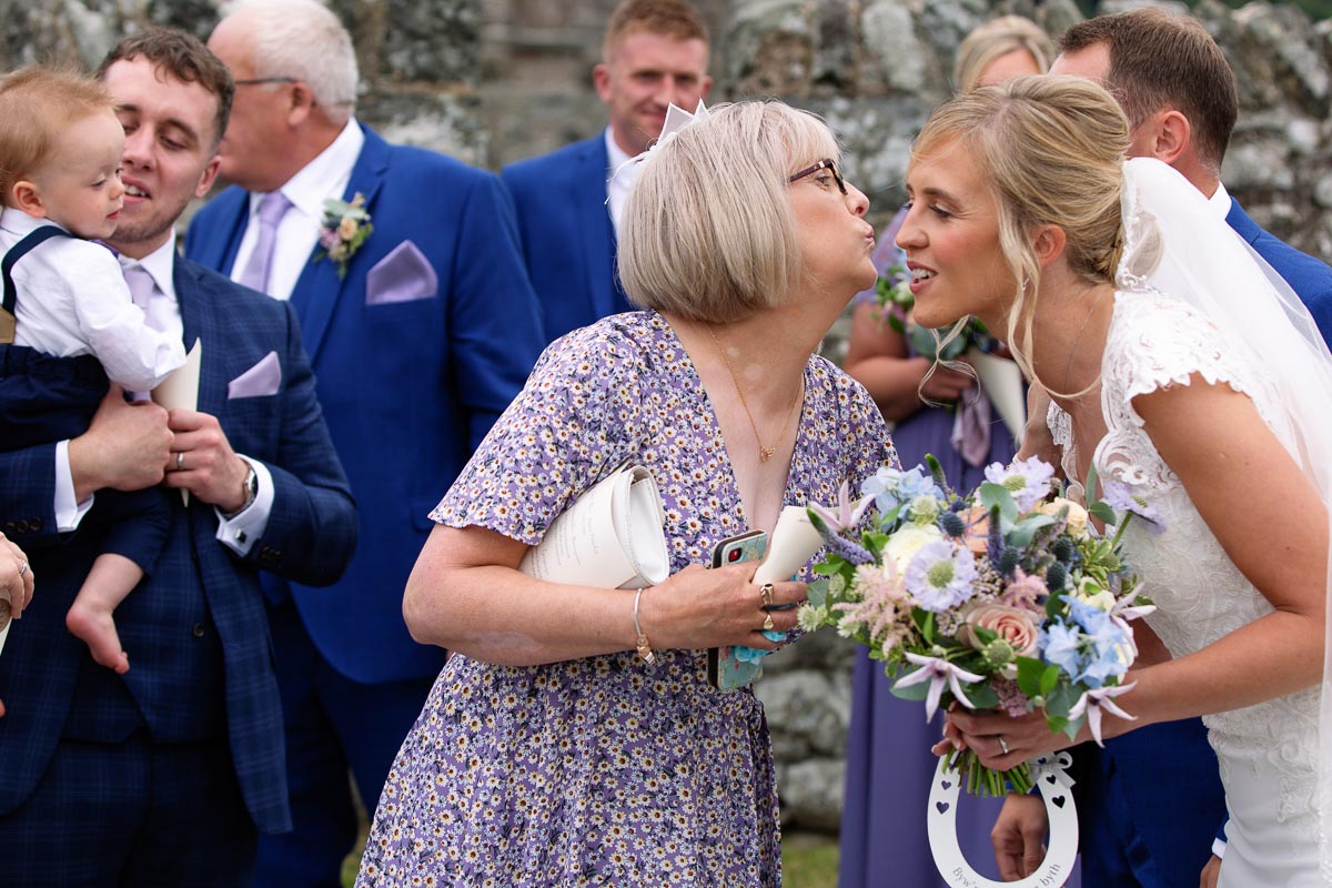 a friend reaching the kiss the brideat St. Mary's Church , Caerhun by Anglesey wedding photographer Gill Jones Photography