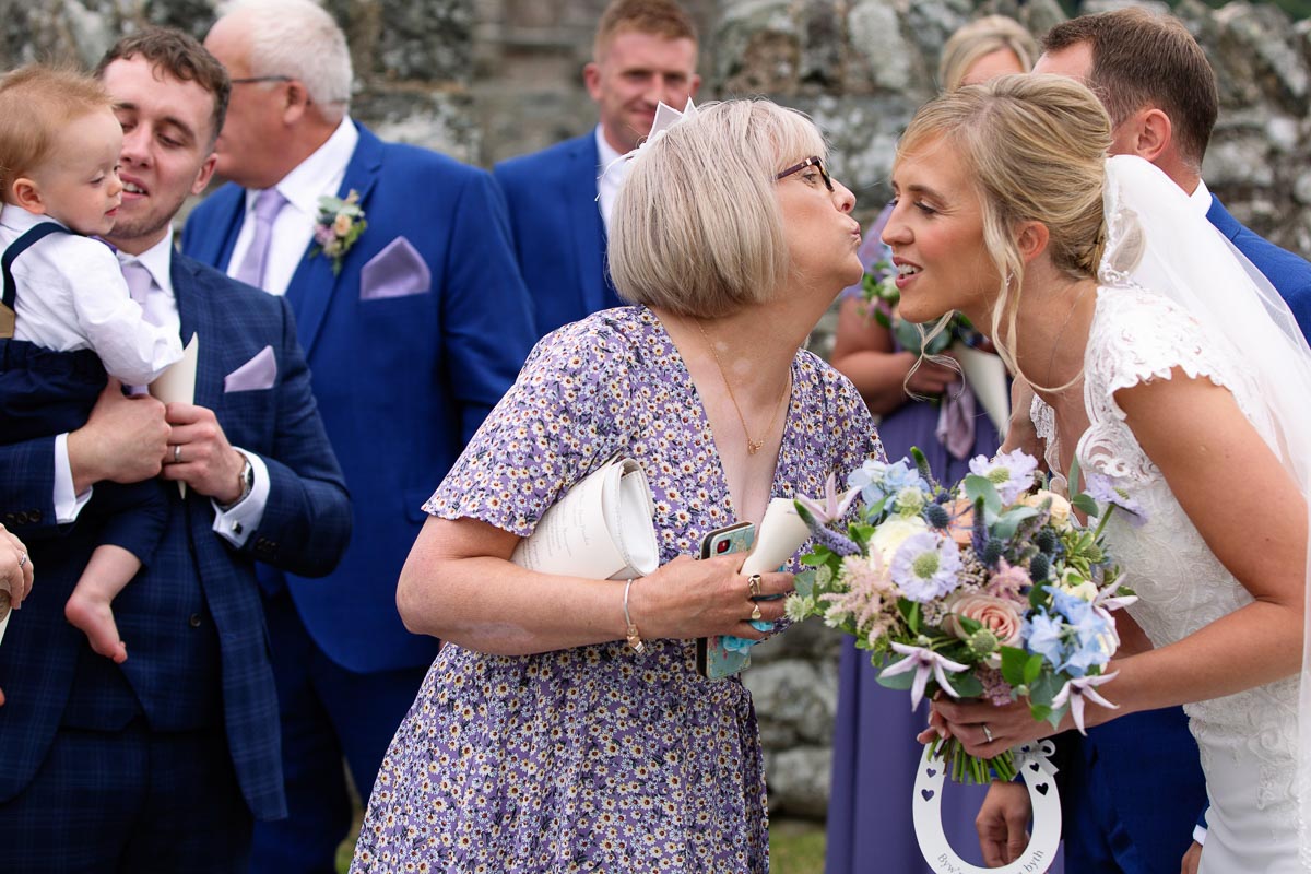 Bodnant Welsh Food Wedding_Rhian and Gethin_013 a friend reaching the kiss the brideat St. Mary's Church , Caerhun by Anglesey wedding photographer Gill Jones Photography
