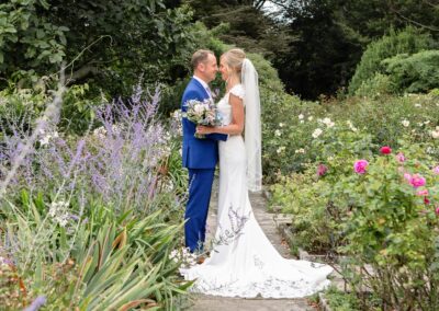 bride and groom standing nose to nose in the rose garden at Bodnant Gardensby Anglesey wedding photographer Gill Jones