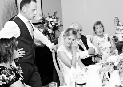 the bride wipes a tear from her eye during the groom's speech at Bodnant Food Centre byby Anglesey wedding photographer Gill Jones