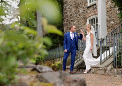 the groom guides his bride down the steps of The Furnace House at Bodnant Food Centreby Anglesey wedding photographer Gill Jones