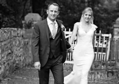 groom hand in hand with bride in front of Furnace Farm house by Anglesey wedding photographer Gill Jones