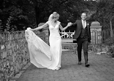 bride guiding the groom as they walk past the Furnace Farmhouse at Bodnant Food Centreby Anglesey wedding photographer Gill Jones