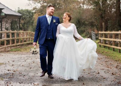 bride and groom laughing whilst walking on farm track at Henblasby Anglesey wedding photographer Gill Jones Photography