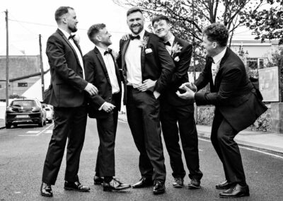 groom and groomsmen larking around outside The Sandy Mount House by Anglesey wedding photographer Gill Jones Photography