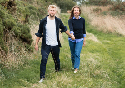 Newly engaged couple walking in field on Anglesey by Anglesey wedding Photographer Gill Jones Photography