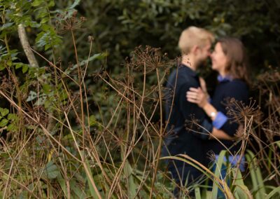 Couple embracing in the distance, seed heads in foreground in sharp focus by Anglesey wedding Photographer Gill Jones