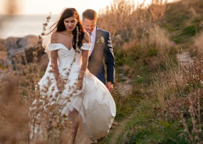 Bride and groom walking on the cliffs in Trearddur Bay at sundownby Anglesey wedding photographer Gill Jones Photography