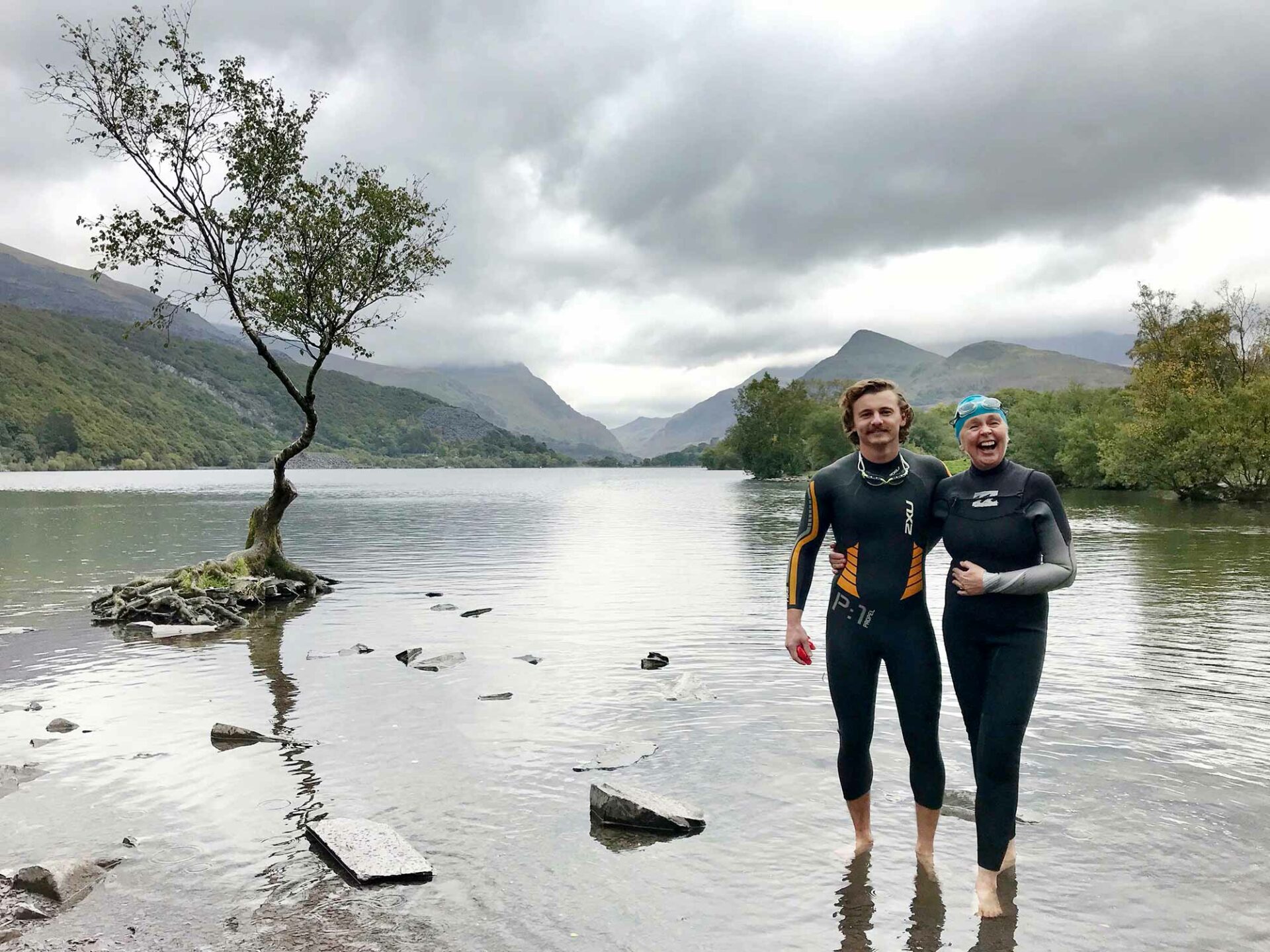 mother and son wearing wetsuits standing by the lone tree at Llyn Padarn by Anglesey wedding photographer Gill Jones