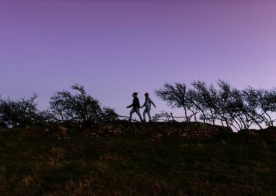 couple walking hand in hand along a dry stone wall at dusk by Anglesey wedding Photographer Gill Jones
