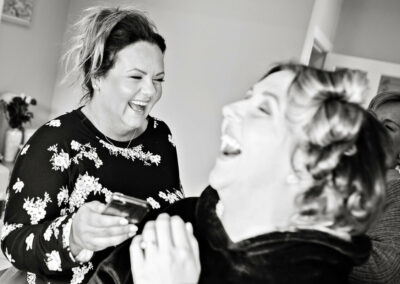 a bridesmaid shows the bride something on her mobile phone and everyone laughs by Anglesey wedding photographer, North Wales, Gill Jones Photography