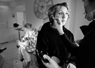 the bride has her make up applied as a bridesmaid open a gift in the background by Anglesey wedding photographer, North Wales, Gill Jones Photography