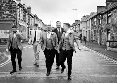 the groom and groom's men walk towards the church laughing by Anglesey wedding photographer, North Wales, Gill Jones Photography