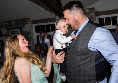 young bridesmaid laughing as father holds his tiny son who has a tie tied around his head by Anglesey wedding photographer, North Wales, Gill Jones Photography Gill Jones Photographer