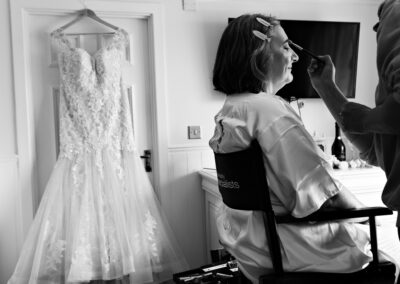 bride having her makeup applied with her dress hanging in the background
