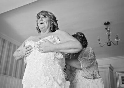 bride being helped into her dress by her bridesmaid, holding the bodice against her